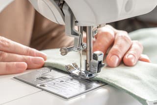 Female hands stitching white fabric on modern sewing machine at workplace in atelier. Women's hands sew pieces of fabric on a sewing machine close-up. Handmade, hobby, small business concept