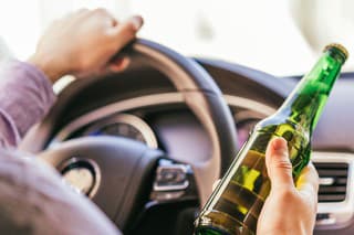 man holding a beer bottle alcohol while driving the car