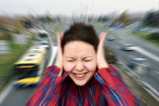 Woman with closed eyes covering her ears in the street while vehicles are passing by fast in the background. Stressful and frustrating situation. Noise pollution concept. Radial blur filter applied.