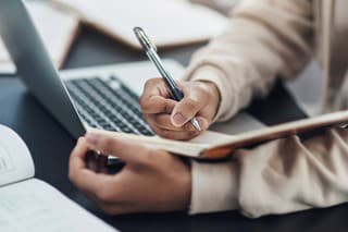 Shot of an unrecognisable man writing in a notebook while working from home