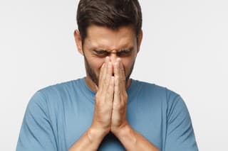Sick young man covering face with hands, sneezing, isolated on gray background