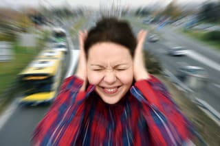 Woman with closed eyes covering her ears in the street while vehicles are passing by fast in the background. Stressful and frustrating situation. Noise pollution concept. Radial blur filter applied.