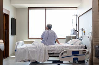 The senior adult woman sits alone in her hospital room while she waits for her daughter.