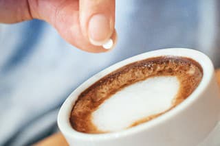 Closeup of unrecognizable woman putting one piece of artificial sweetener into her coffee. These sweeteners are based on aspartame or acesulfam compunds . Tilt shot.