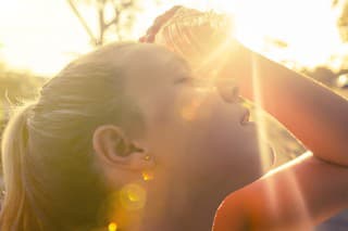 Woman using water bottle to cool down. Fitness and wellbeing concept with female athlete cooling down on a city street. She is holding a water bottle to her head to cool down. The sun is low creating long shadows and some lens flare. Copy space