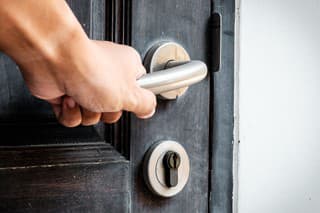 Hand opening a wooden door by turning an aluminum door knob in counter clockwise direction