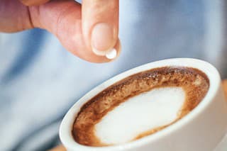 Closeup of unrecognizable woman putting one piece of artificial sweetener into her coffee. These sweeteners are based on aspartame or acesulfam compunds . Tilt shot.