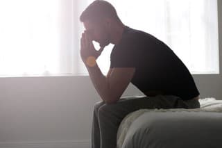 A man sitting at the end of a bed, deep in solemn thought.