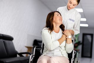 Happy woman on wheelchair is hugging doctor for halping in clinic