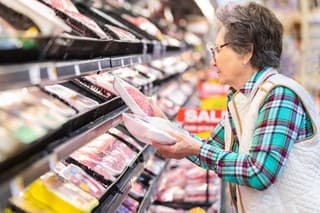 Senior woman comparing prices for meat selection.