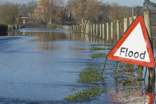 A flood warning sign, on a closed country road next to water logged fields in the Avon Valley, Hampshire, England. Flooded after an extreme amount of rainfall at the start of 2014