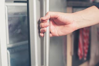 The hand of a young man is opening a freezer door