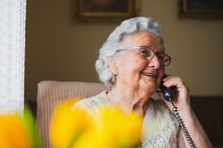 Old lady speaks to her daughter and son by telephone, and she is rejoicing because they are coming to visit her soon.