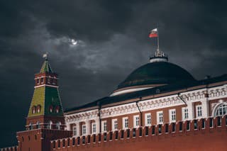 Night shot: Kremlin Moscow Dome of Senate building, a red Kremlin wall, flag of Russia with the emblem on it; sinister dark sky with a moon partly closed by the clouds