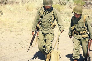 Two soldiers walking along a dusty road. Vintage, authentic army uniforms and weapons.