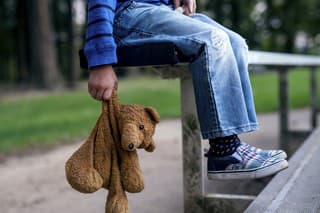 Young boy holding teddybear while alone on the bleachers