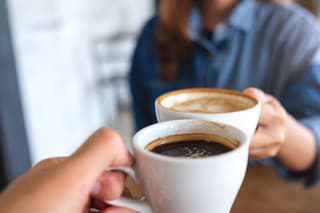 Closeup image of a woman and a man clinking coffee cups together in cafe