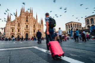 People are visiting Milan, Italy. Blurred motion. A man with a red suitcase in foreground. Milan Cathedral in the background.