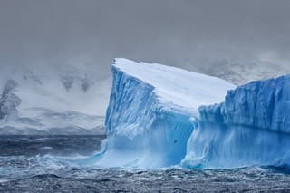 Massive Iceberg floating in the Southern Ocean in Antarctica with snow covered mountains in the background