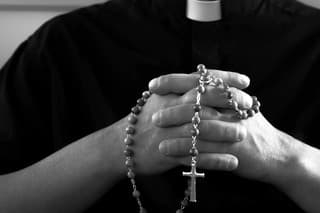 Silhouette of a praying priest with rosary beads in hands