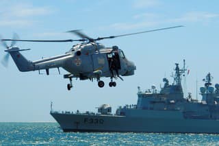 Setubal, Portugal: Portuguese Navy Super Lynx Mk.95 helicopter with diver on the door, approaching frigate F330, NRP Vasco da Gama, built by Westland Helicopters. Portuguese Naval Aviation. Two Lynx can be operated from the flight deck of a Vasco da Gama-class frigate.