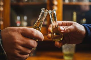 Close up on hands of two unknown men toasting with traditional serbian drink plum brandy rakija slivovitza holding glass called cokance at home