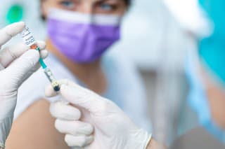 Doctor's hands in surgical gloves pulling COVID-19 vaccine liquid from vial to vaccinate female patient