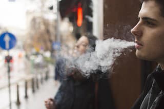 Young man smoking a cigarette in front a building in a city street