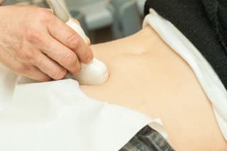 Image of mid adult woman having abdominal ultrasound. Close up of her belly with doctor's hand and ultrasound. selective focus.