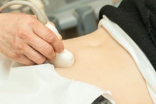 Image of mid adult woman having abdominal ultrasound. Close up of her belly with doctor's hand and ultrasound. selective focus.