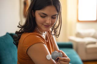 Young diabetic patient teenage woman using applicator to attach glucose sensor on arm.