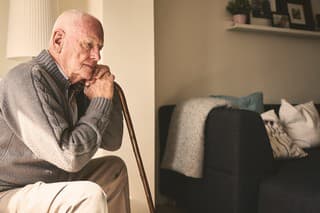 Thoughtful elderly man sitting alone at home with his walking cane