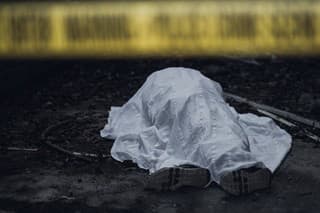 The dead body is seen lying on the ground behind a cordon tape.