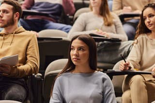 Large group of university students paying attention on a lecture at amphitheater. Focus is on woman in the foreground.