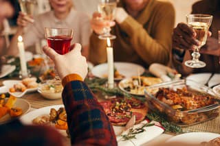 Close up of modern adult people raising glasses while enjoying Christmas dinner at home, copy space