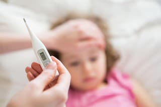 Close-up thermometer. Mother measuring temperature of her ill kid. Sick child with high fever laying in bed and mother holding thermometer. Hand on forehead.