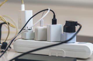 Electrical outlet with many chargers connected to it for a smartphone, laptop, microphone.