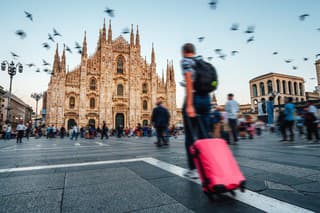 People are visiting Milan, Italy. Blurred motion. A man with a red suitcase in foreground. Milan Cathedral in the background.