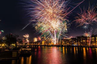 Colorful array of fireworks seen reflected in the water on the river, late at night near midnight. Celebration of the new year in a big European tourist/tourism city.