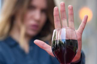 A woman at the table gestures with her hand to refuse a glass of red wine