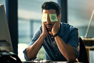 Shot of a tired young businessman working late in an office with adhesive notes covering his eyes