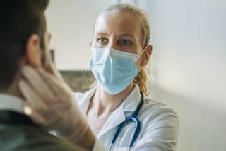 Female doctor wearing surgical mask examining infected patient. Mature healthcare worker checking mid adult man. They are at pharmacy.