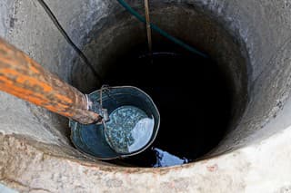 an iron bucket on a wooden stick with water at the depth of an old round well