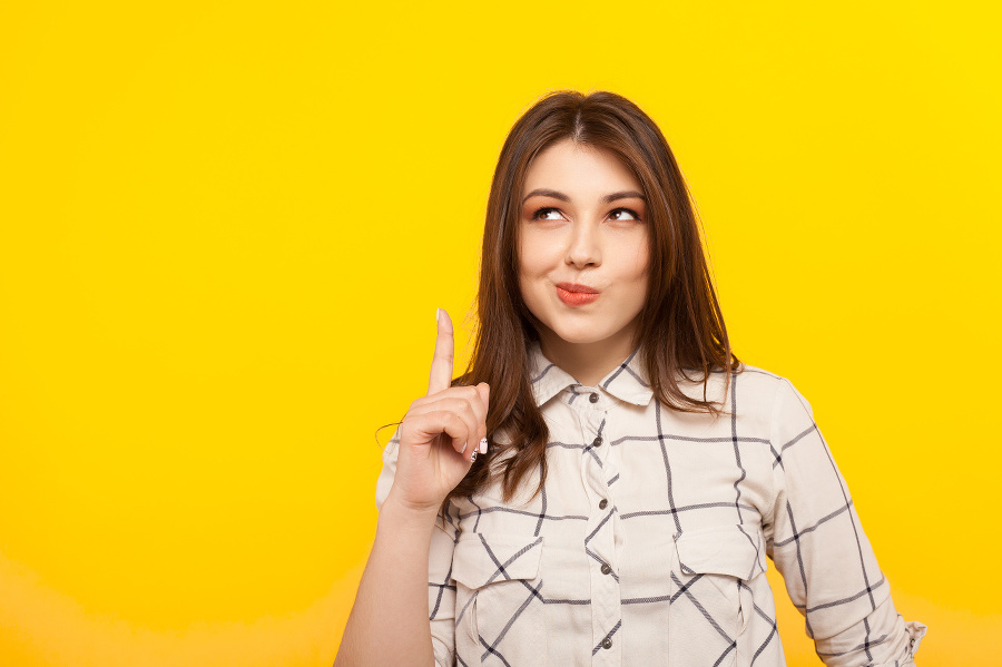 Pensive young girl thinking and pointing up on the yellow background.