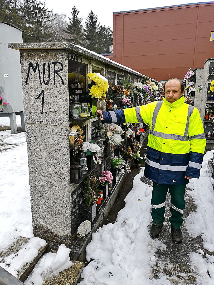Robotník Andrej stojí pri nahnutej a poškodenej stene s urnami v kolumbáriu.