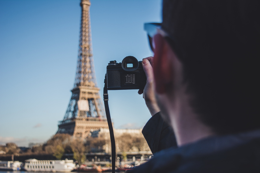 One man, standing on the street in Paris on a beautiful day, taking pictures of Eiffel Tower, rear view.