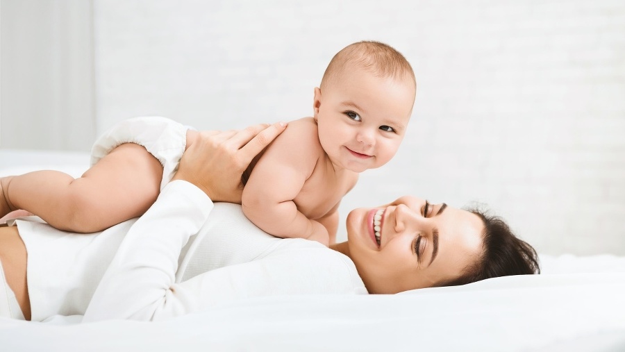 Family having fun together. Mom and baby boy in diaper playing in bedroom, panorama, copy space