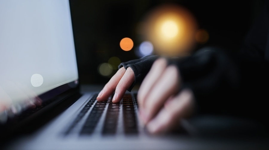 Shot of an unrecognizable computer hacker using a laptop late at night