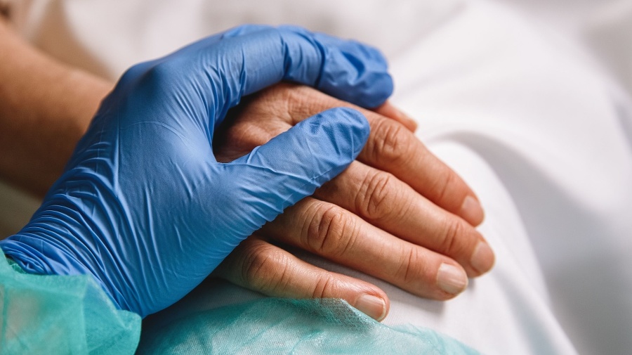 Close up of a doctor hand with blue glove giving support and love to a patient at hospital. Coronavirus pandemic concept.