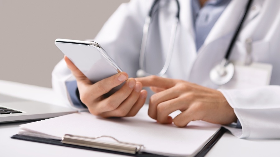 Consultation Online. Unrecognizable male doctor using smartphone at workplace, messaging with his patient, prescribing treatment